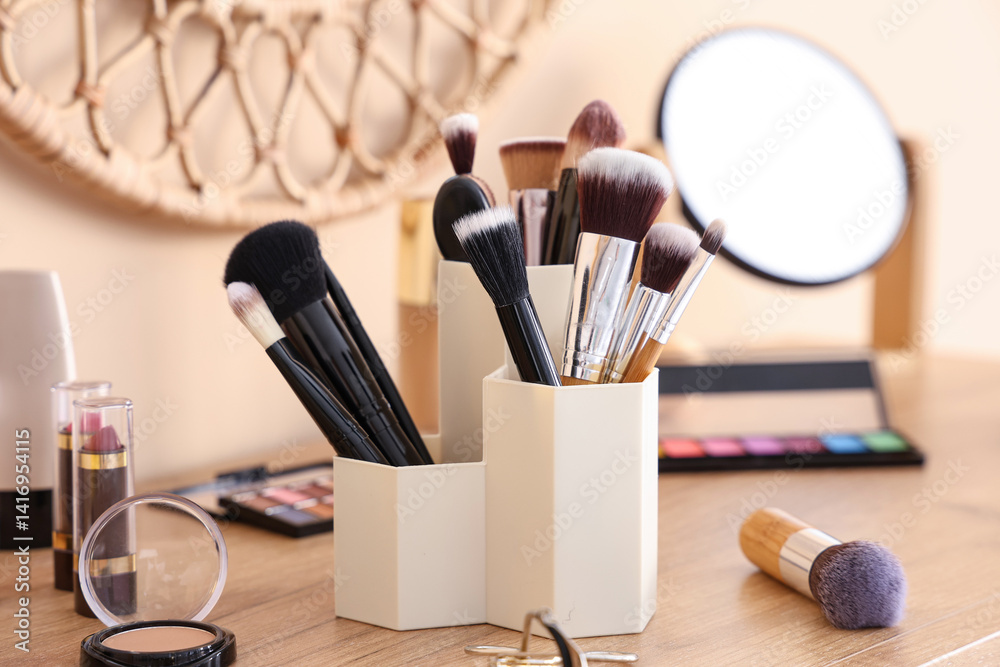 Holder with makeup brushes and different decorative cosmetics on chest of drawers at home