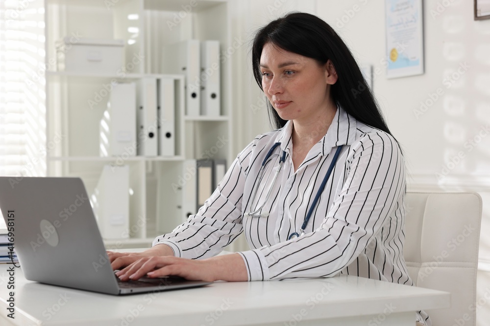 Professional doctor working with laptop at white desk in hospital
