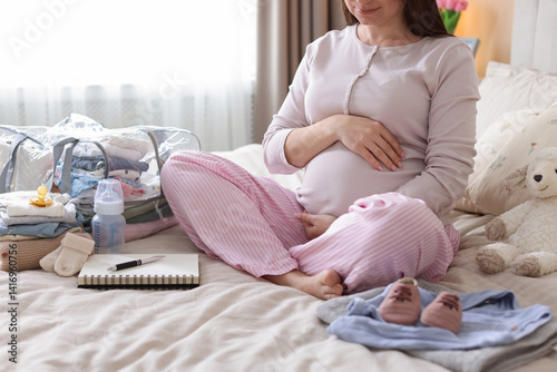 Pregnant woman on bed with baby stuff to bring into maternity hospital at home, closeup