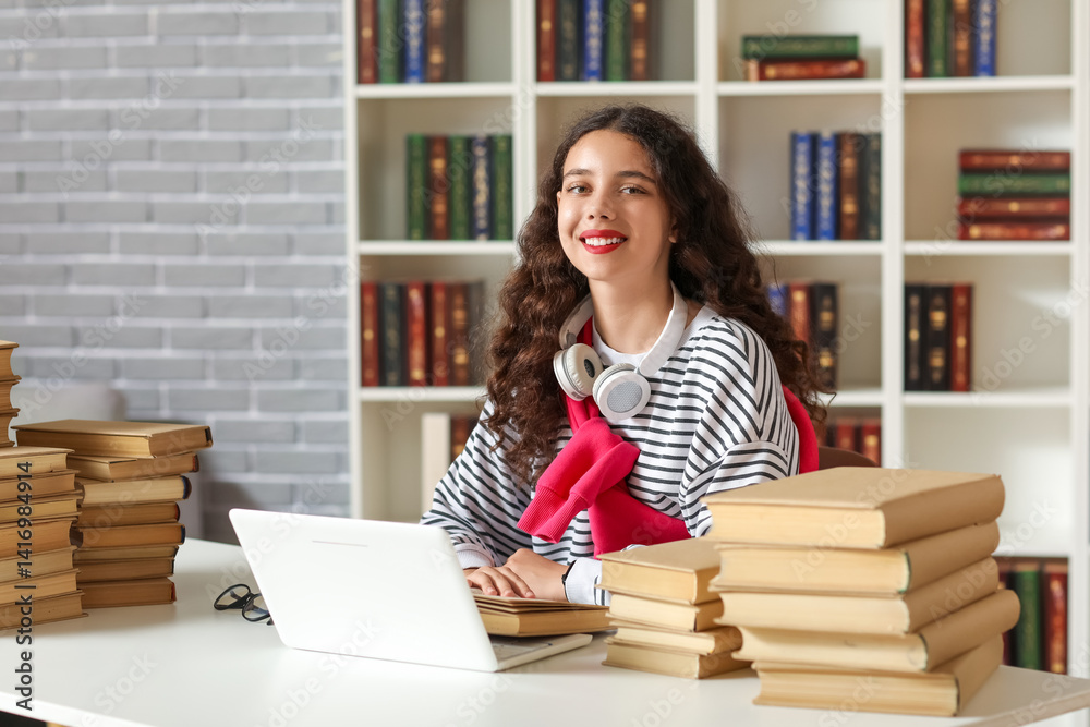 Female student using laptop at table with stack of books in library