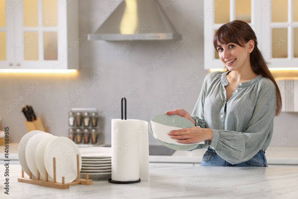 Woman wiping plate with paper towel at white marble table in kitchen Woman wiping plate with paper towel at white marble table in kitchen