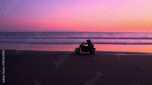 Driving motorbike along the beach in Bali at purple sunset, light reflecting on the ocean waves, feeling freedom and vacation vibe, independence. Couple ride motorcycle along the shore