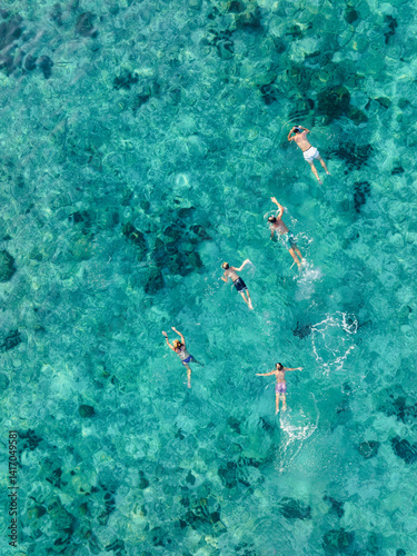 Top-down view of a group of people swimming over a vibrant coral reef in shallow tropical waters near Phi Phi Island, Thailand.