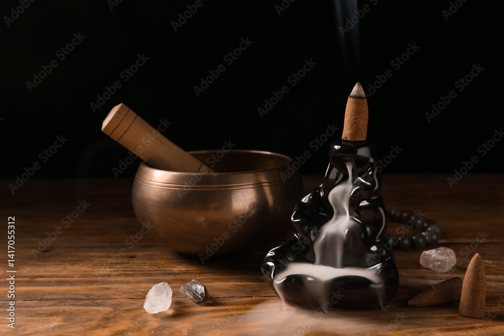Backflow incense holder with smoldering cone, crystals and Tibetan singing bowl on dark wooden table