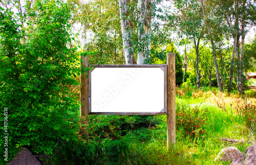 Wooden advertising or information billboard in the forest path. Mock up Wood board inside the trees. Outdoor nature.