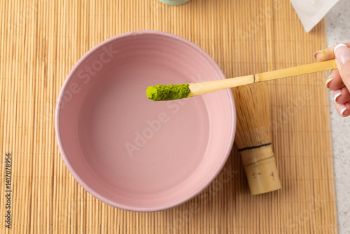 Woman preparing matcha green tea powder with bamboo spoon and whisk