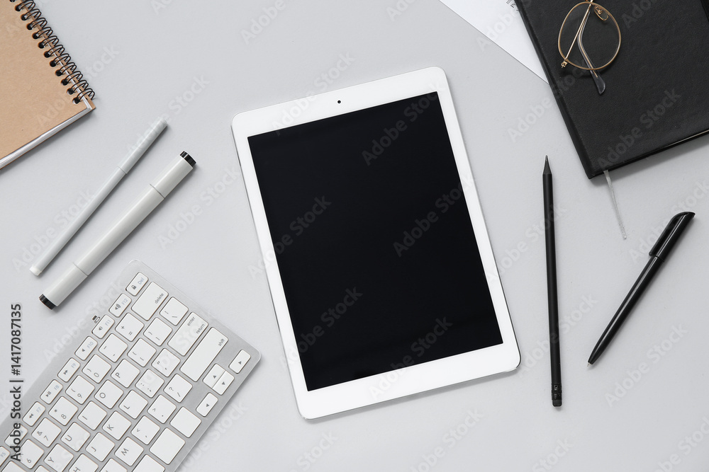 Composition with modern tablet computer, keyboard and stationery on grey background Composition with modern tablet computer, keyboard and stationery on grey background