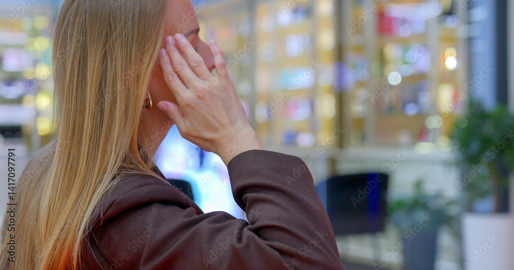 Fototapeta premium Stressed woman covers face with hands while standing in shopping mall.