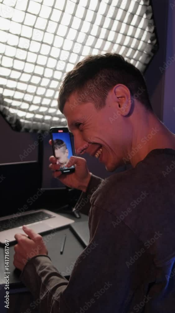 Male blogger content creator laughing after a failed take and restarting video recording with smartphone, realistic behind the scenes moment of content creation at home. RGB lighting. Vertical video