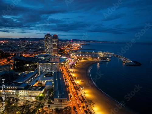 Nighttime view of palm-lined beach road and marina lit with golden lights