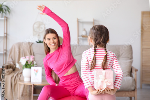 Obraz na płótnie Cute little girl with gift box behind back surprising her exercising mother at home. Mother Day celebration w salonie