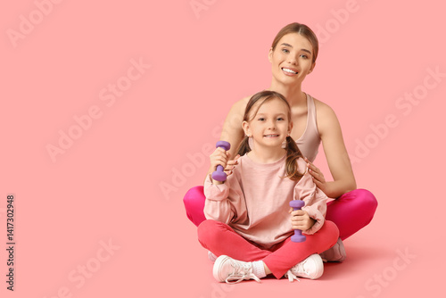 Sporty young mother and her cute little daughter with dumbbells sitting on pink background. Mother Day celebration