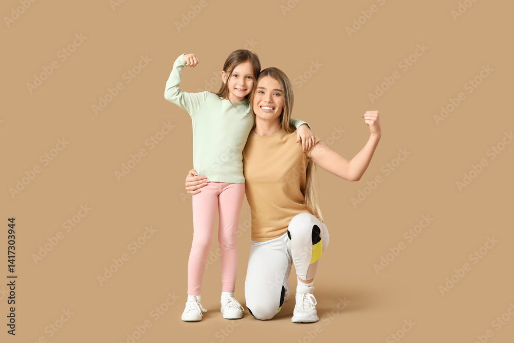 Sporty young mother and her cute little daughter showing muscles on beige background. Mother Day celebration