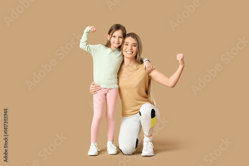 Obraz na płótnie Sporty young mother and her cute little daughter showing muscles on beige background. Mother Day celebration w salonie