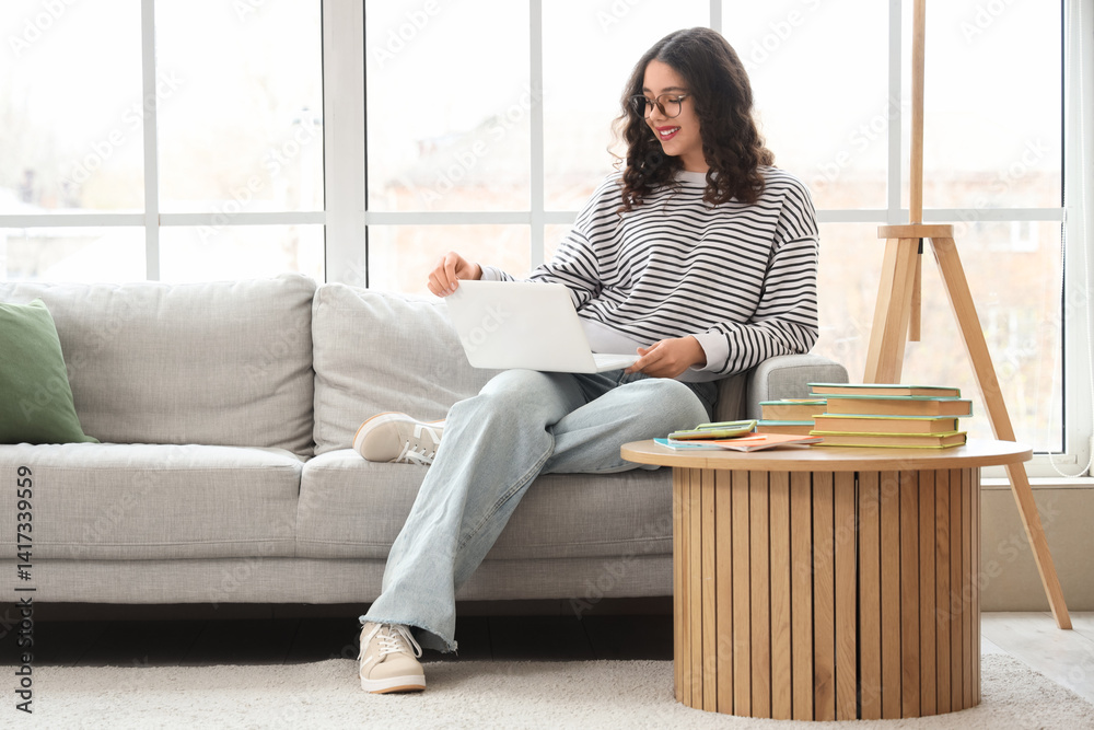 Female Indian student studying with laptop on sofa at home