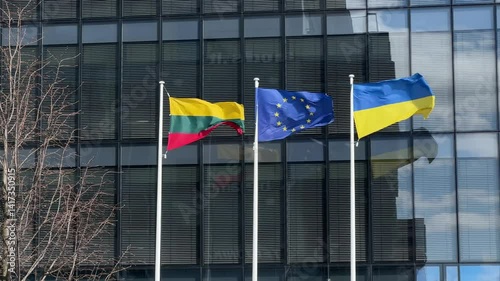 Lithuanian, European Union, and Ukrainian flags waving in front of modern glass building