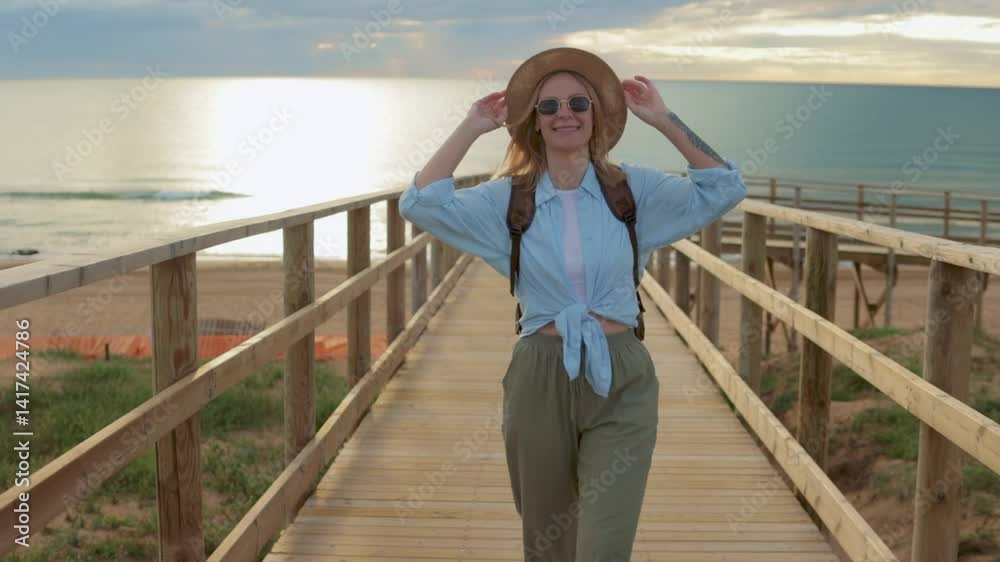 Relaxed woman traveler with sunglasses. Straw hat walking wooden boardwalk.Travel, weekend, relax and lifestyle concept Relaxed woman traveler with sunglasses. Straw hat walking wooden boardwalk.Travel, weekend, relax and lifestyle concept