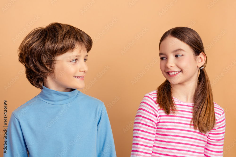 Two smiling children looking at each other, one in a blue shirt, the other in pink stripes, on a beige background Two smiling children looking at each other, one in a blue shirt, the other in pink stripes, on a beige background