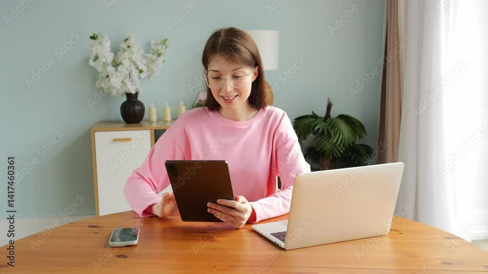 Engaged in digital activities, a woman smiles while using her tablet beside a laptop and phone. Engaged in digital activities, a woman smiles while using her tablet beside a laptop and phone.