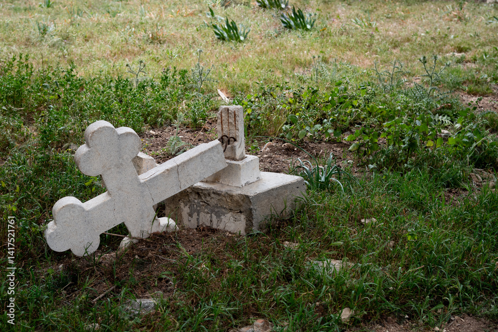 Fallen cross lying on grass symbolizing loss and grief. Ruined orthodox cemetery