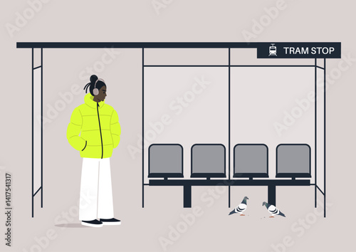 A teenager stands at a cozy tram stop in a vibrant yellow puffer jacket, surrounded by quietness, empty seats, and curious pigeons pecking at the ground