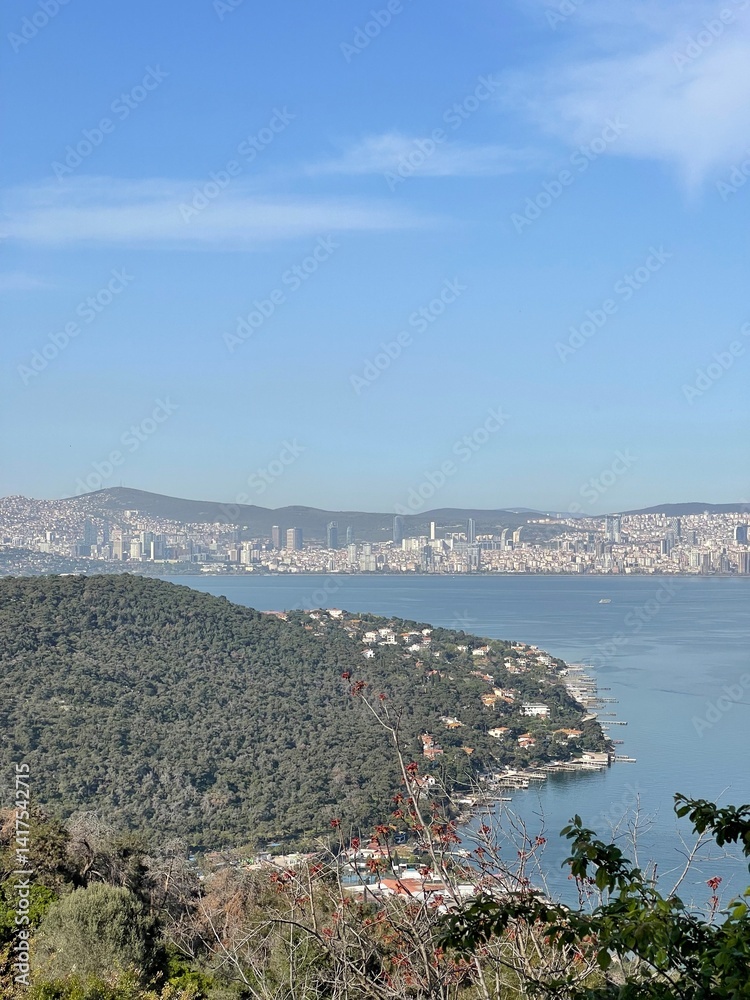 Obraz premium High angle view of the coast with a bay and densely populated urban area visible in the distance, representing a city on the sea and a distant city skyline