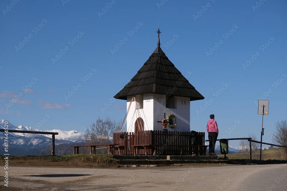 Viewpoint of High Tatras and Bialskie Tatras on Pass over Lapszanka with old white chapel and silhouette of woman in pink jacket.