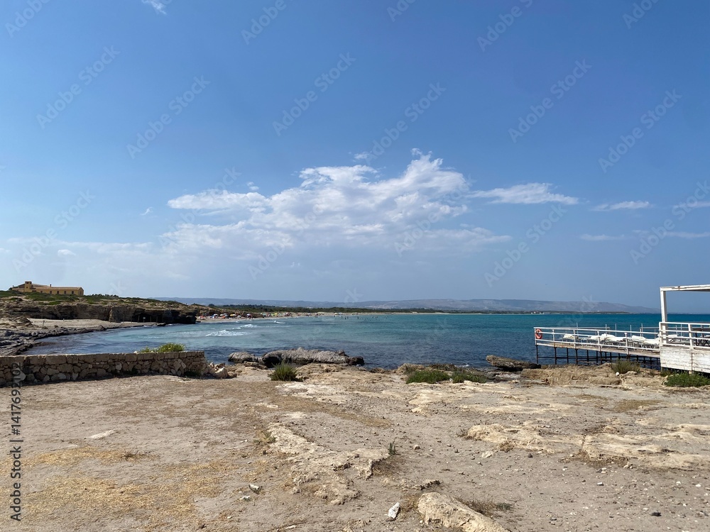 Noto coastline featuring sandy beach, rocky shoreline, azure waters stretching beneath clear summer skies in southeastern Sicily Noto coastline featuring sandy beach, rocky shoreline, azure waters stretching beneath clear summer skies in southeastern Sicily