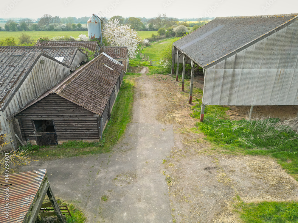 Drone view of an abandoned dairy farm showing large hay barns as well as a distant milking parlour and grain silo for cow feed.