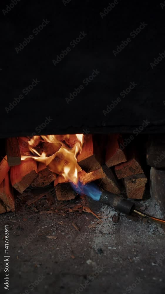 Flame from torch igniting stacked firewood under smoker