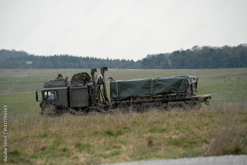 Soldier lookout in the cab of British army MAN SV HX 8x8 eight wheeled logistics truck carrying supplies across countryside