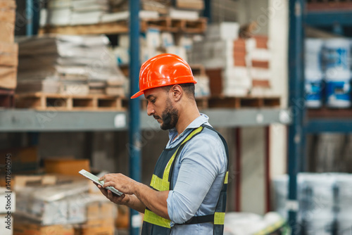 caucasian warehouse worker checking using tablet. caucasian man wearing safety examine storage area with touch screen document. supervisor wear helmet safety vest at workplace inspect stock by tablet