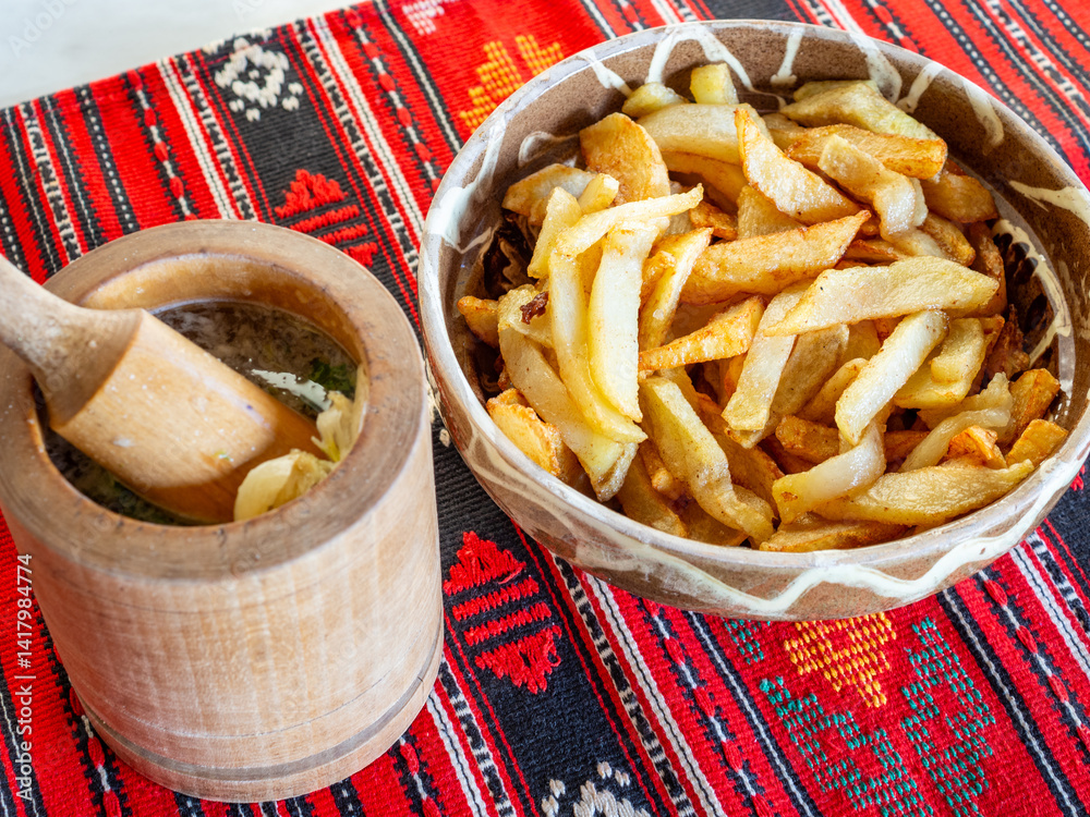 fried french fries in bowl with crushed garlic in wooden mortar