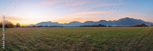 Wide grassy field at sunset with distant mountains
