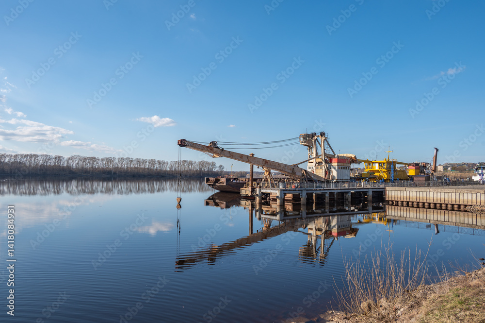 A floating crane, tugboats and a barge at a pier on a river. A floating crane, tugboats and a barge at a pier on a river.