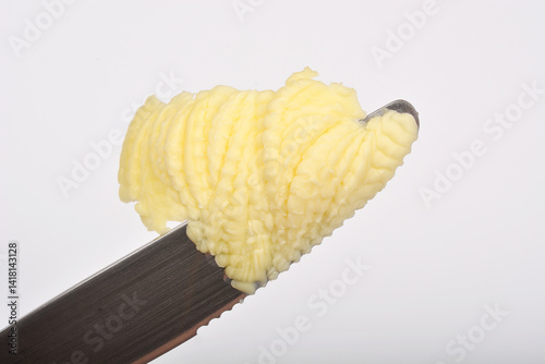 A close-up shot shows a curl of yellow butter on a serrated knife blade against a blurred white background