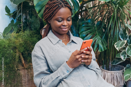 Obraz na płótnie A young woman is focused on her smartphone in a cozy indoor space filled with greenery w salonie