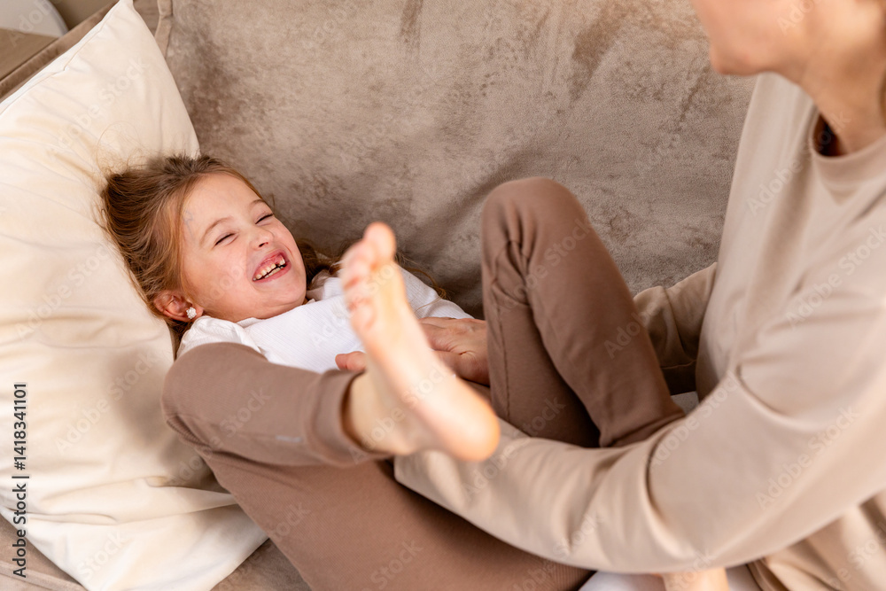 Close up hands of mom tickling kid daughter, laughing together on couch. Cheerful mother playing funny game with little cute girl at home, having fun, relaxing. Happy family. High quality photo