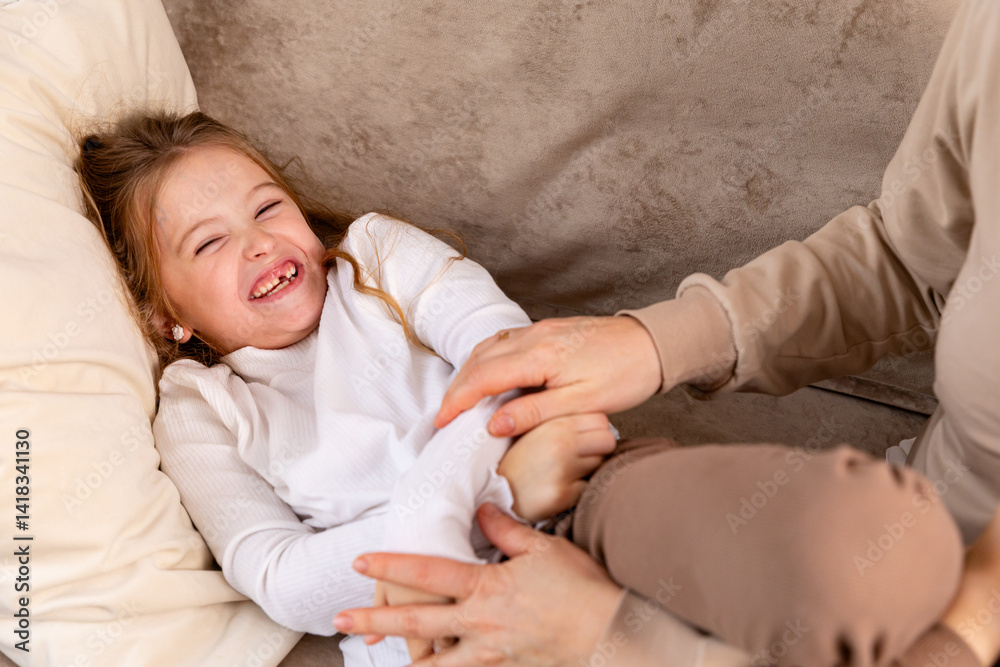 Close up hands of mom tickling kid daughter, laughing together on couch. Cheerful mother playing funny game with little cute girl at home, having fun, relaxing. Happy family. High quality photo