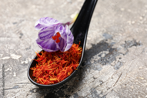 Fototapeta Naklejka Na Ścianę i Meble -  Spoon with dried saffron threads and crocus flower on grey grunge table