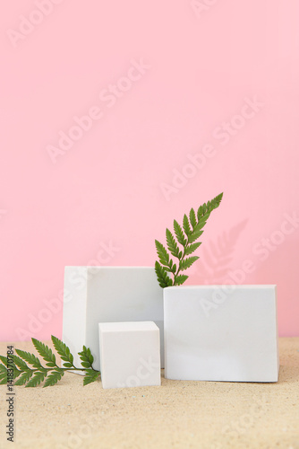 Decorative plaster podiums with fern leaves on sand against pink background