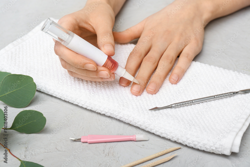 Female hands applying cuticle oil onto fingernails, towel and eucalyptus twig on grey grunge background