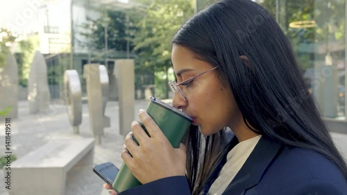 Native American woman with Hispanic features and Chilean descent, standing sideways in a business environment, drinking from a mug and checking her phone, with a corporate city skyline in the backgrou