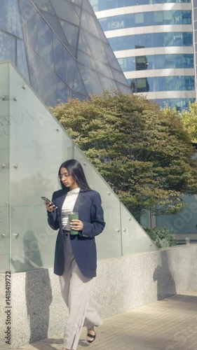 Slow-motion shot of a Native American woman with Hispanic features and Chilean descent, wearing glasses, a navy blazer, white pants, and black heels, walking and checking her phone in a corporate offi