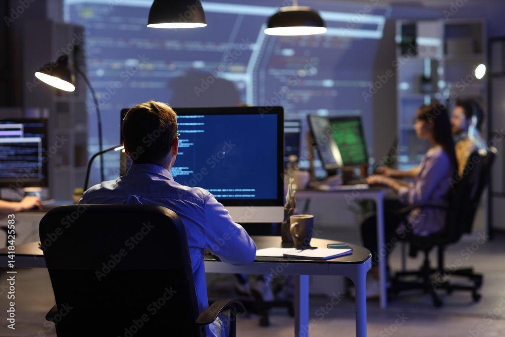 Fototapeta premium Male programmer working with his team in office at night, back view
