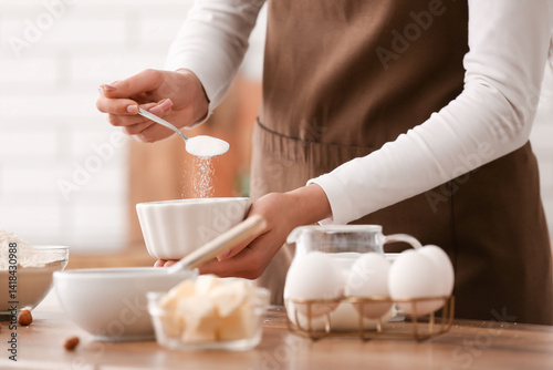Woman adding sugar into bowl for preparing chocolate brownie at table in kitchen. Closeup
