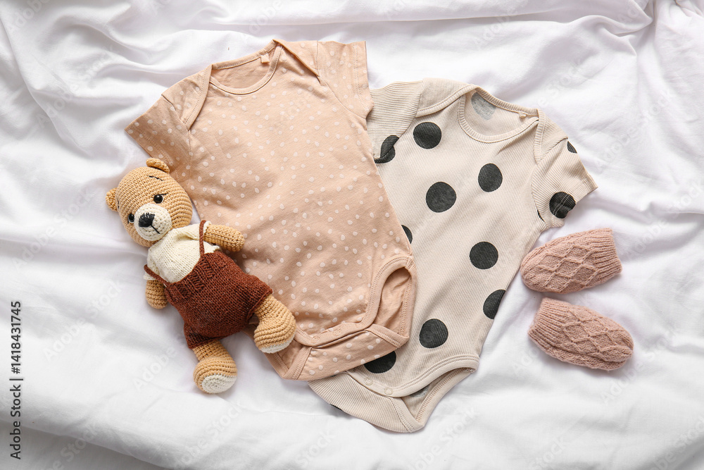 Baby clothes and knitted teddy bear on light bed