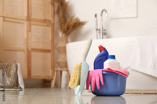 Plastic basin with cleaning supplies on floor in bathroom