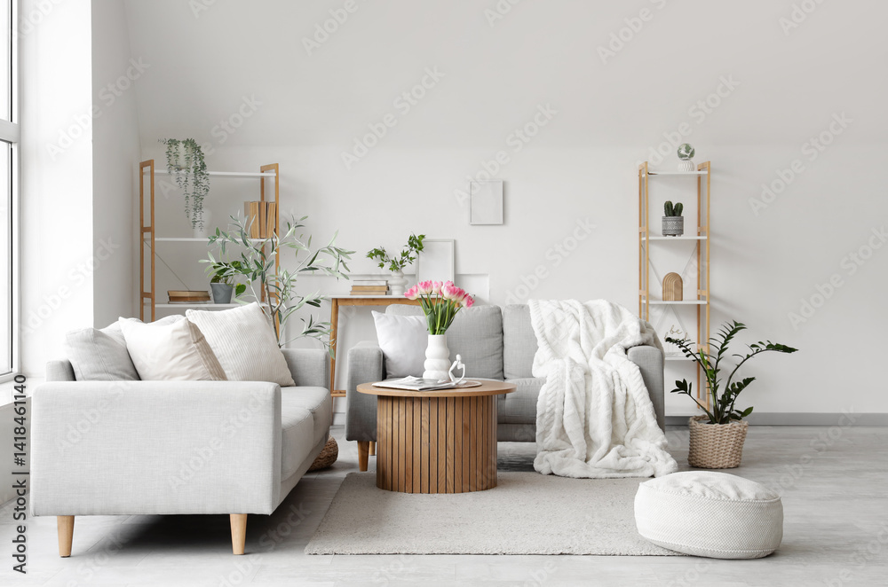 Obraz premium Interior of light living room with grey sofas, shelf units and plants