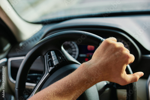 Close up of a hand gripping a steering wheel inside a car cabin, indicating motion and driving experience